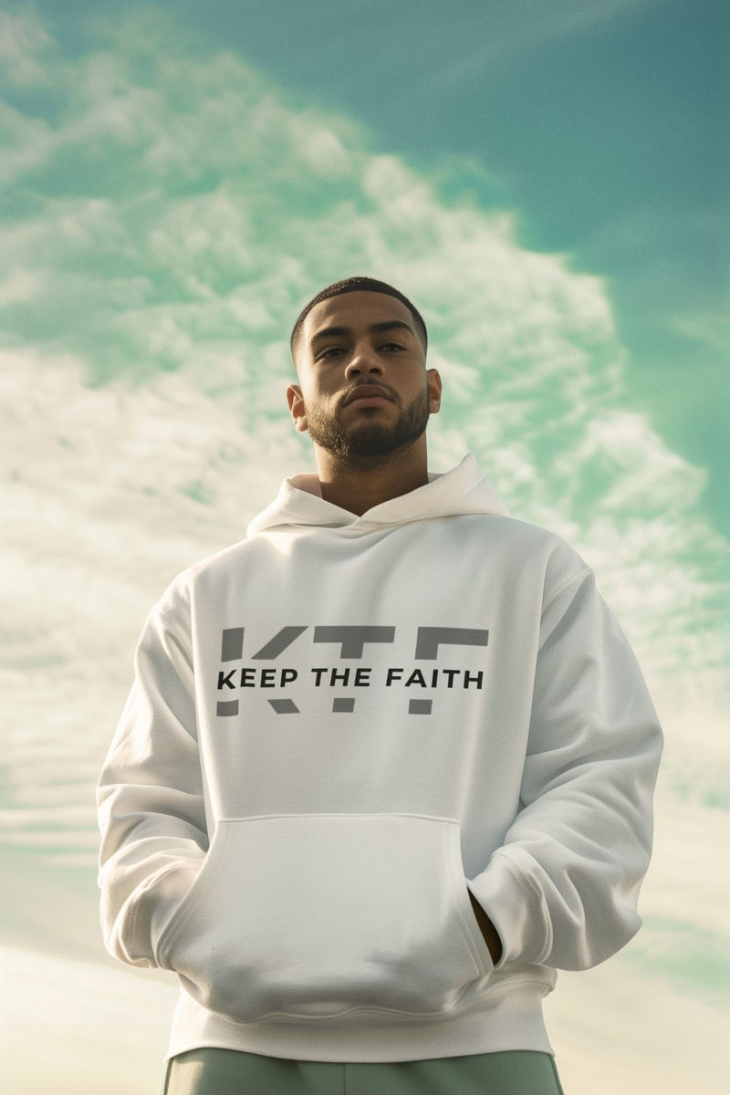 Man wearing Keep The Faith white hoodie standing outdoors under blue sky