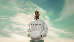 Man wearing Keep The Faith white hoodie standing outdoors under blue sky.